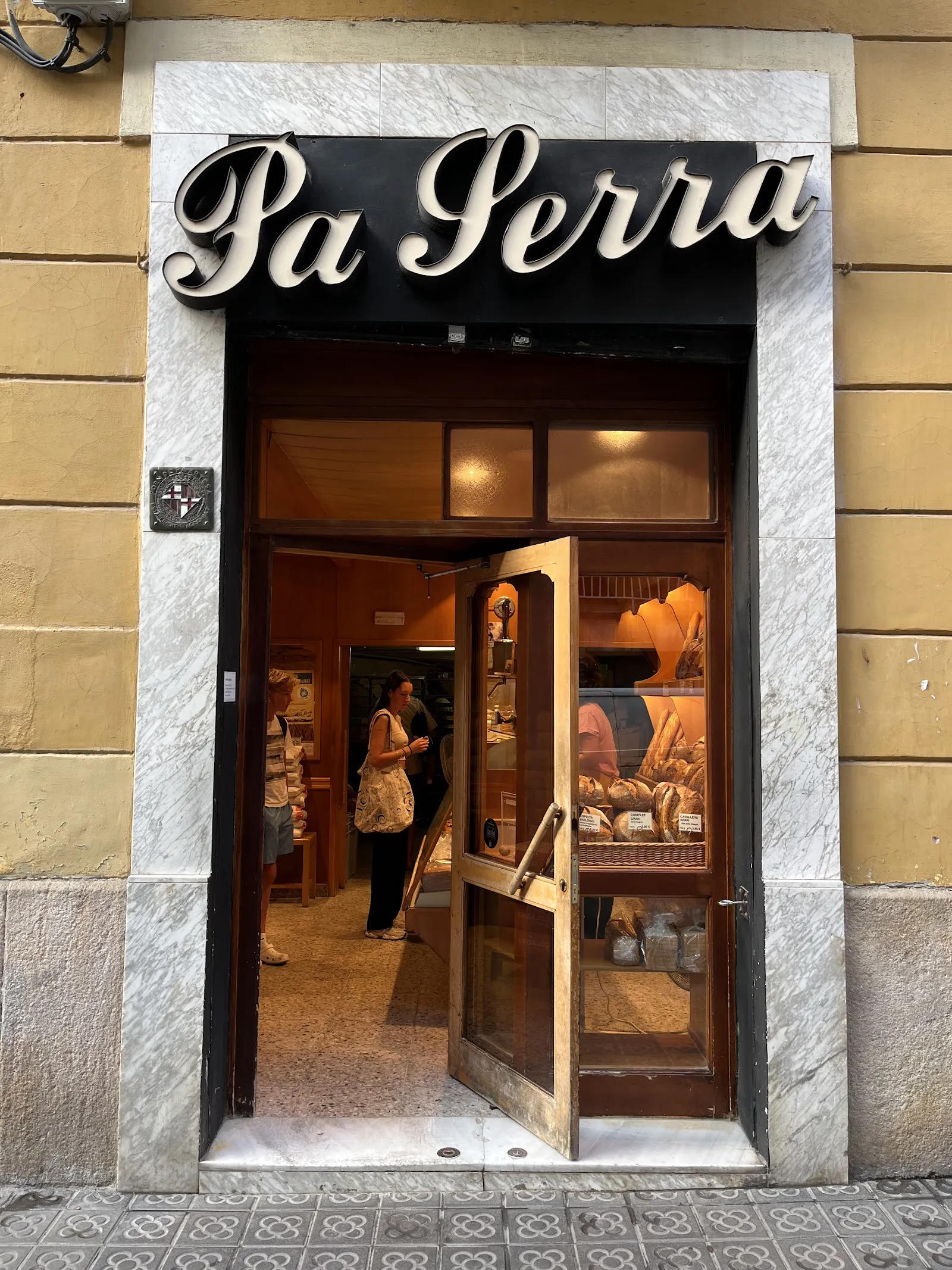La porta del Forn Pa Serra, amb el rètol negre i la façana groga